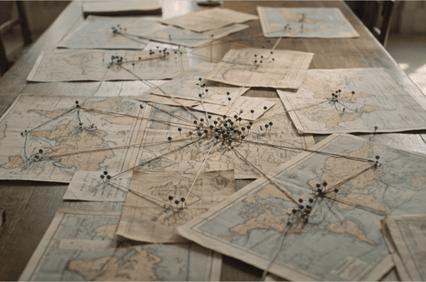 A collection of vintage maps spread out on a table, interconnected with pins and strings.