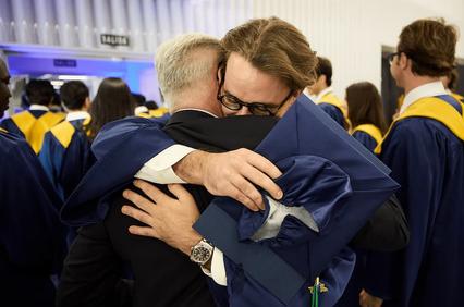 A heartfelt embrace between two graduates in caps and gowns.