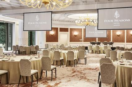 An elegant banquet hall featuring round tables and large screens.