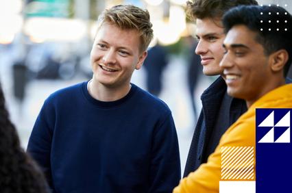 Three young men, smiling and engaging in a conversation on a city street.