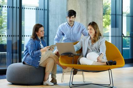Three professionals, two women and one man, discussing over a laptop in a modern office setting