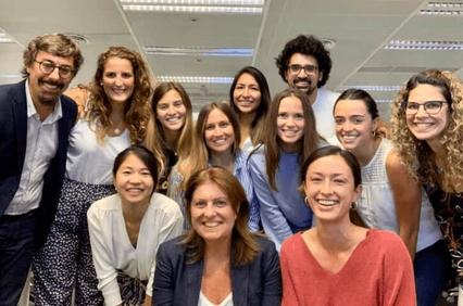 A group of twelve smiling people posing for a photo in an office environment.