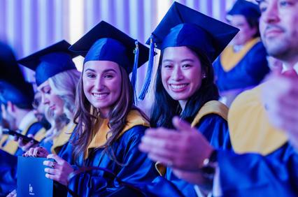 Two smiling graduates in caps and gowns at a ceremony.