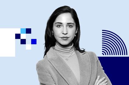 A young woman in a stylish blazer poses confidently against a minimalist blue background.