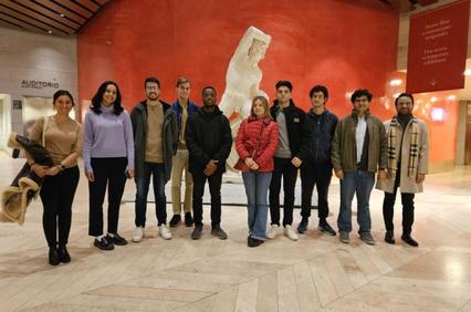 A group of ten people posing in an indoor setting with a statue in the background.