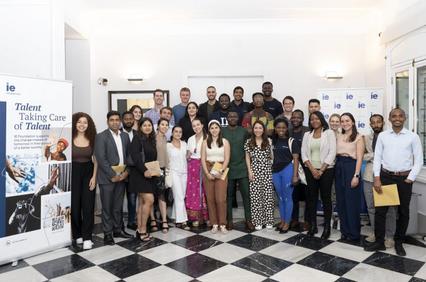 A group of diverse people posing for a photo in a room with a checkered floor and promotional banners.