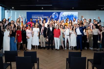 A group of people celebrating at a graduation ceremony in a modern room with large windows.