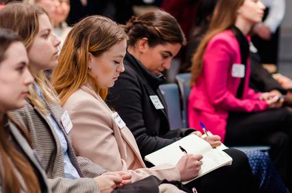 A group of young adults attentively listening and taking notes at a conference.