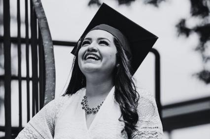 A joyful graduate woman in a cap and gown laughing outdoors.