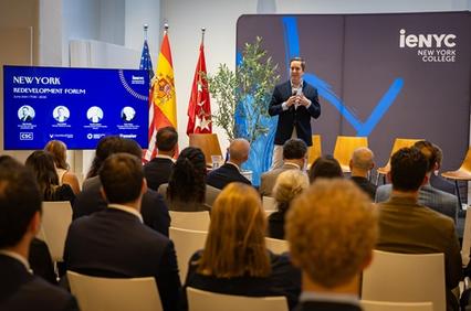 A speaker presenting at the New York Redevelopment Forum with flags in the background.
