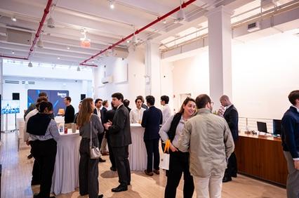 A networking event with a group of people engaged in conversation near a table in a modern venue.