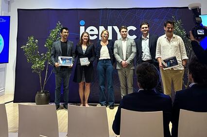 A group of six individuals stands in front of a backdrop at an event, holding awards and smiling.