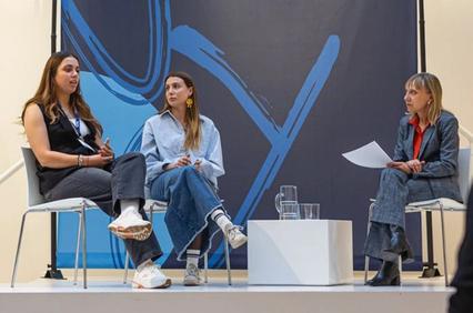 A panel discussion featuring three women seating on chairs with a modern backdrop.