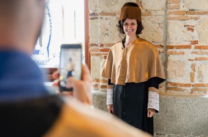 A woman in traditional attire is posing for a photo against a stone wall.