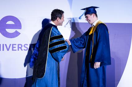 A graduate shakes hands with a professor during a graduation ceremony.
