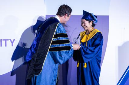 A graduate is receiving a diploma from a professor during a graduation ceremony.