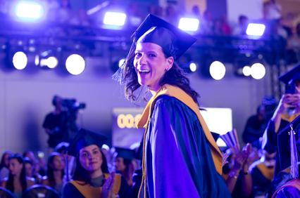 A joyful graduate walks across the stage during a graduation ceremony.