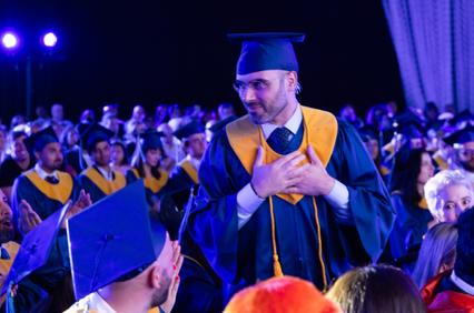 A graduate stands and looks around at a ceremony filled with fellow graduates.