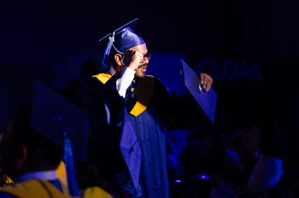 A graduate celebrating and holding their diploma during a ceremony.