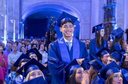 A joyful graduate stands in a crowd during a graduation ceremony.