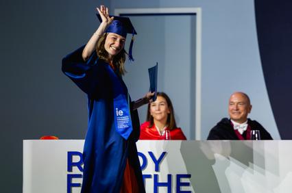 A graduate in a blue gown celebrating during a graduation ceremony.
