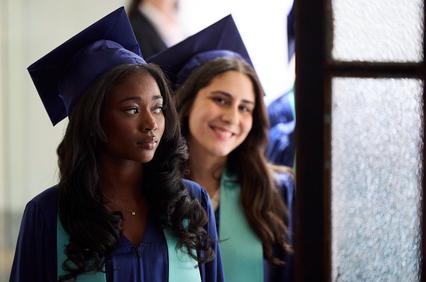 The image depicts two graduates in caps and gowns waiting for a ceremony.