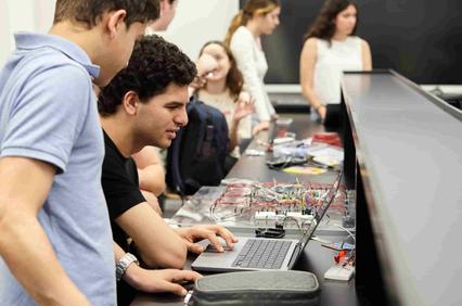 A group of students collaborating on a project with computers and electronic components.