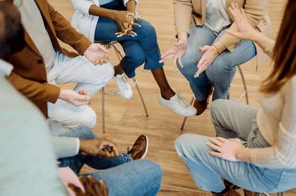 A group of people sitting in a circle, gesturing with their hands during a discussion or activity.