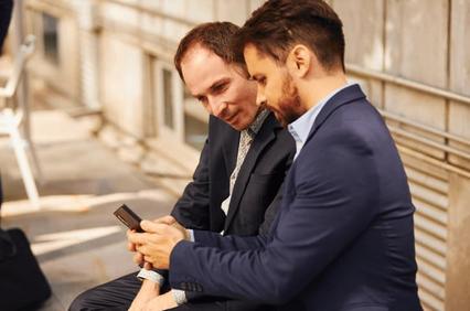 Two men in business suits sitting together and looking at a smartphone.