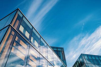 A modern glass building reflecting the blue sky and clouds.