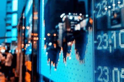 A stock market display board showing financial data in a cityscape at night.