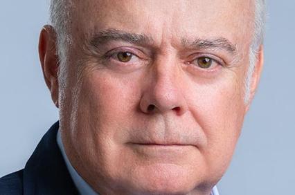 Close-up portrait of an elderly man with grey hair and serious expression, wearing a suit.