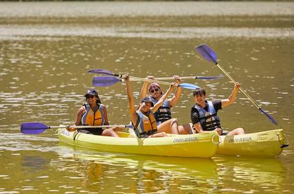 Three people joyfully kayaking on a calm river, waving and smiling.