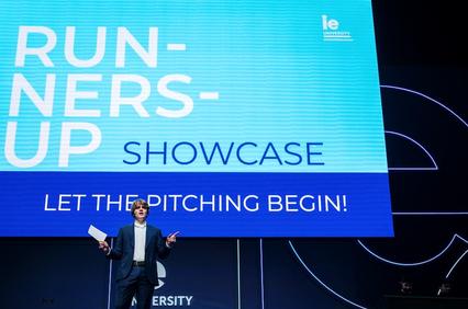 A speaker on stage at a showcase event for runners-up, enthusiastically starting the pitch presentations.