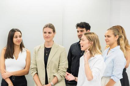 A group of young professionals engage in conversation in a modern office setting.
