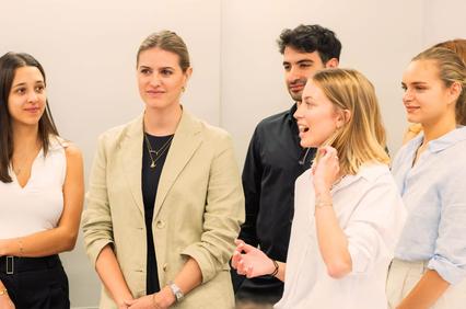 A group of young professionals engaged in conversation in a modern office setting.
