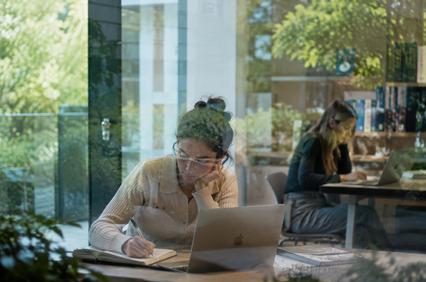 Two women are working on their laptops in a bright and modern office space filled with greenery.