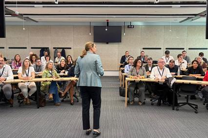 A speaker presents to a large audience in a modern conference room.