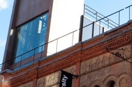 Modern glass addition on top of a classic red brick building with a 'University' banner.