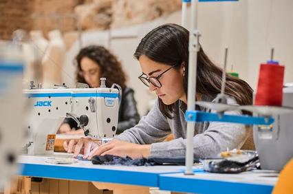 A young woman focused on sewing at a machine in a creative workspace.