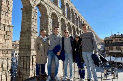 A group of five people posing in front of the ancient Roman aqueduct in Segovia, Spain.