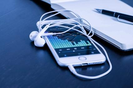 A smartphone with earphones and a graphical sound level on the screen, lying on a dark surface next to a pen.