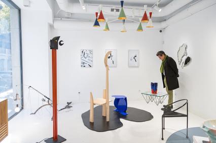 A person browsing an art exhibition with various contemporary sculptures and wall art pieces in a white gallery space.