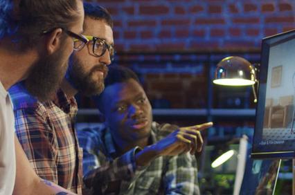 Three men collaborating at a computer workstation in a modern office setting.