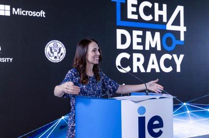 A woman smiles while speaking at a podium with 'Tech4Democracy' and logos of Microsoft and IE University in the background.