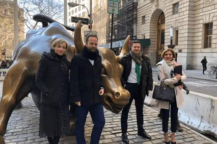 Four people posing next to the Charging Bull sculpture in a city setting.