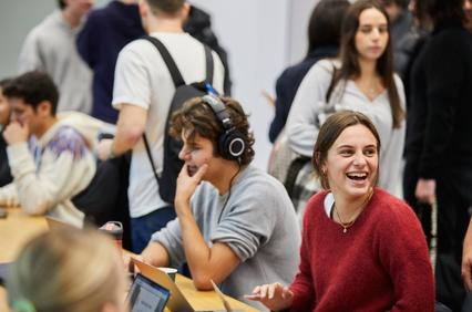 A lively group of students chatting and working on laptops in a casual setting.