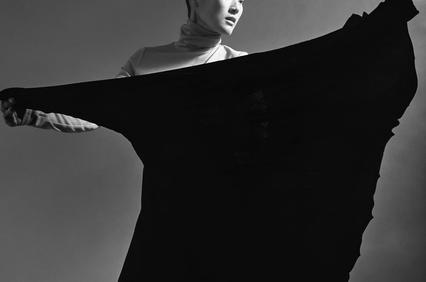 A black and white photo of a woman in a dynamic pose with a flowing black garment.