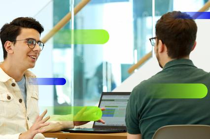 Two young professionals are engaged in a discussion while working on a laptop.