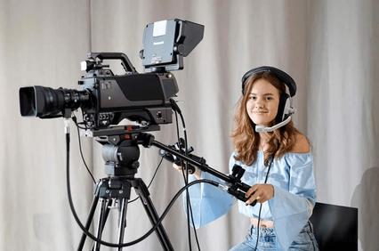 A young girl is operating a video camera while wearing a headset.